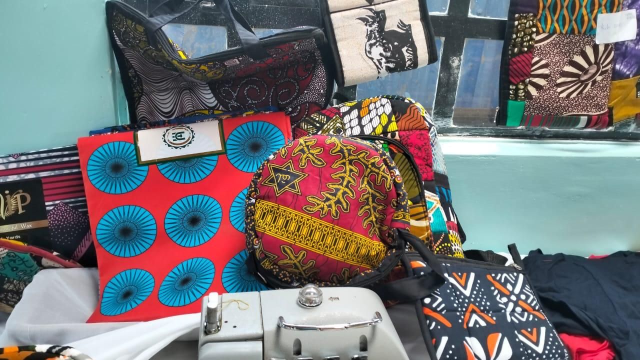 Bags and fabrics made from colourful Ankara print on display next to a sewing machine