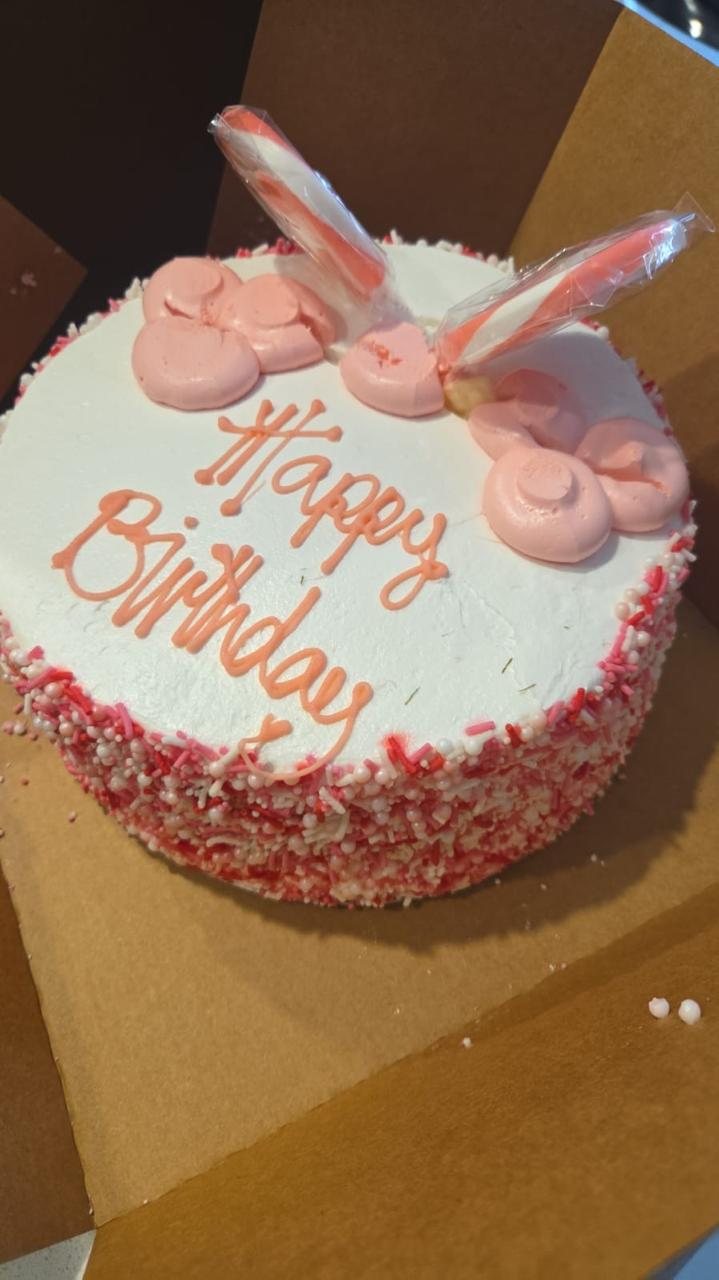 A Happy Birthday cake with pink icing and sprinkles
