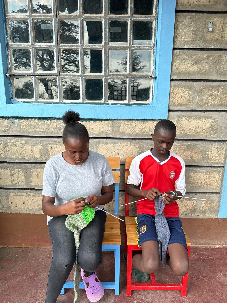 Two children knitting side by side on the veranda