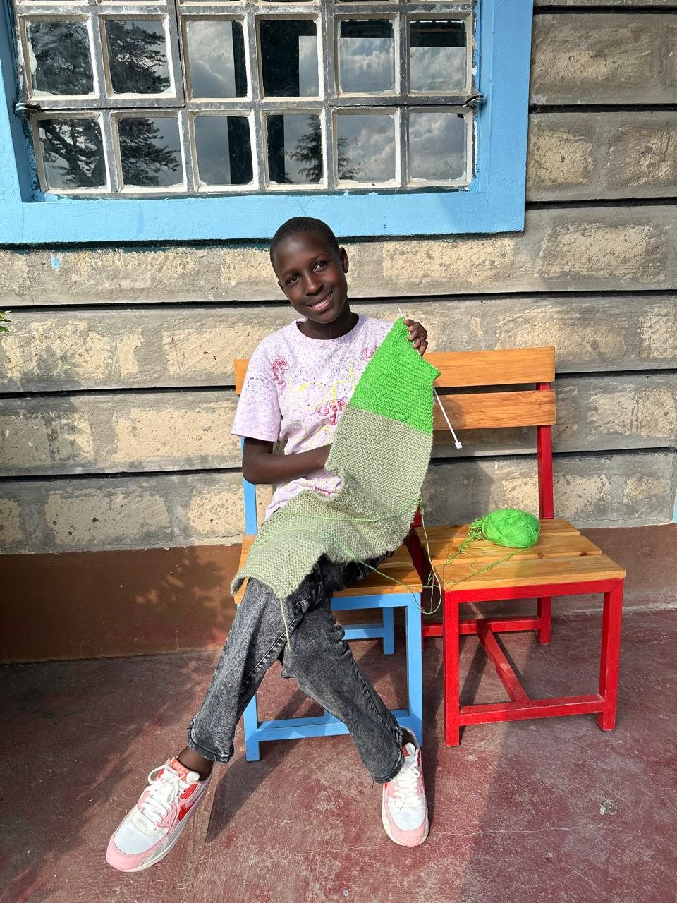A child smiling and holding up a colourful piece of knitting